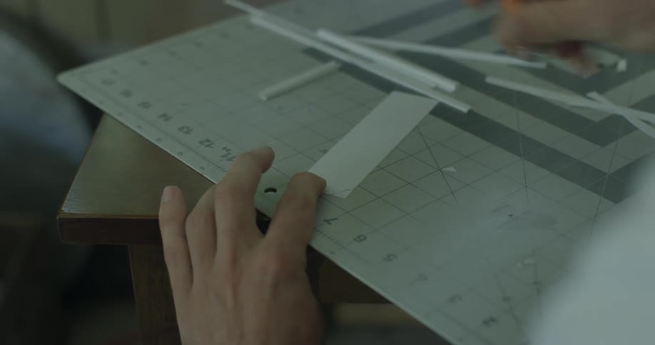A man is using an exacto knife to cut a piece of plastic as he builds a model
