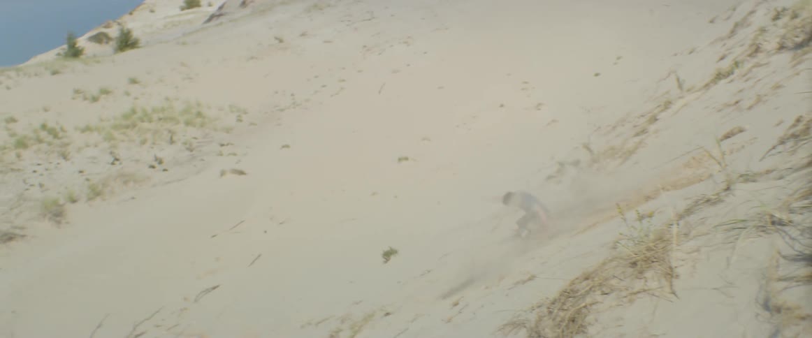 A boy jumps off a ledge and tumbles down a sand slope