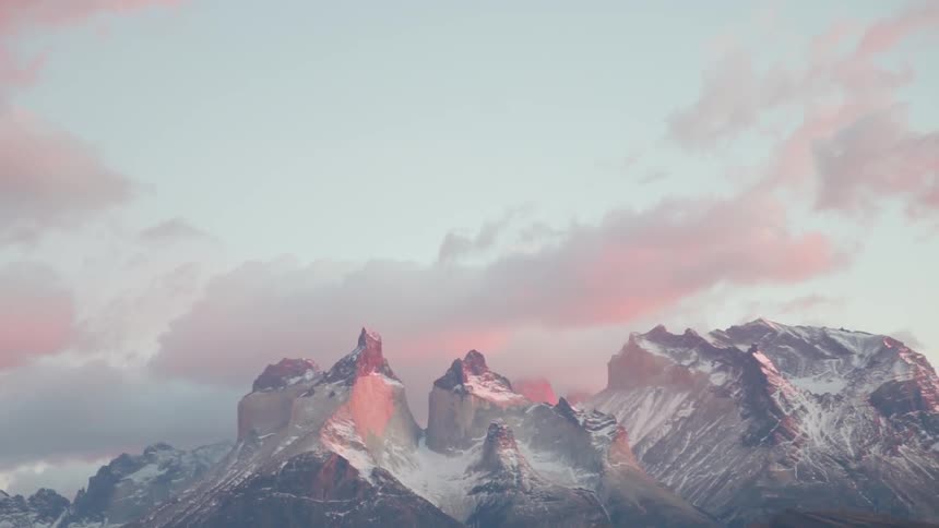 Clouds float above snowy mountains at sunset