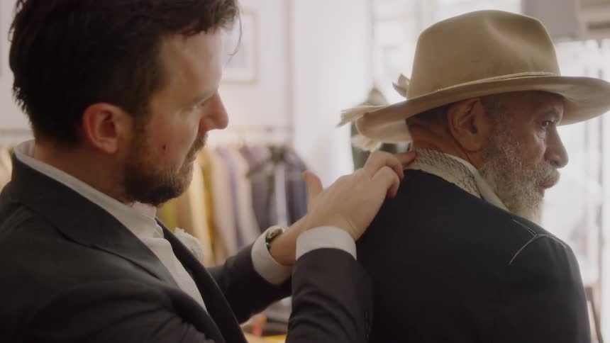 Tailor adjusts bearded man's suit in a store