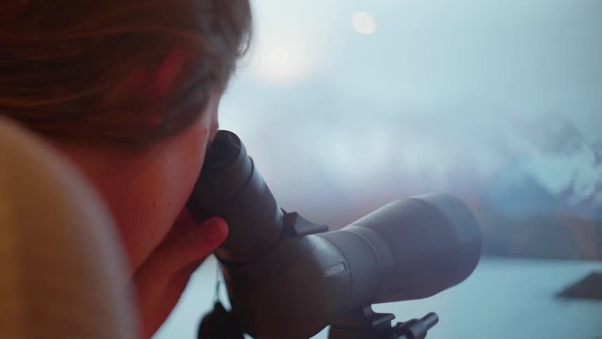 A woman looks at mountains through a telescope