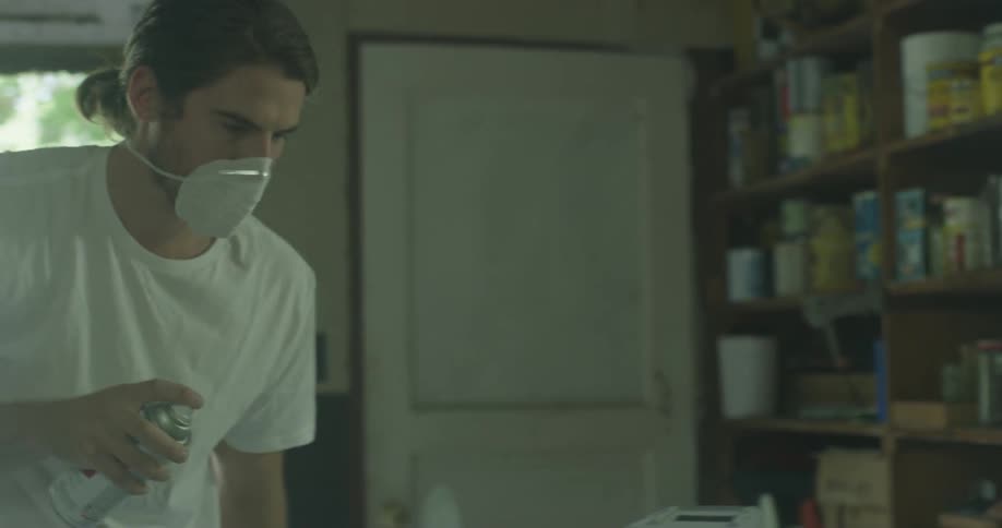 A man wears a mask while using spray paint