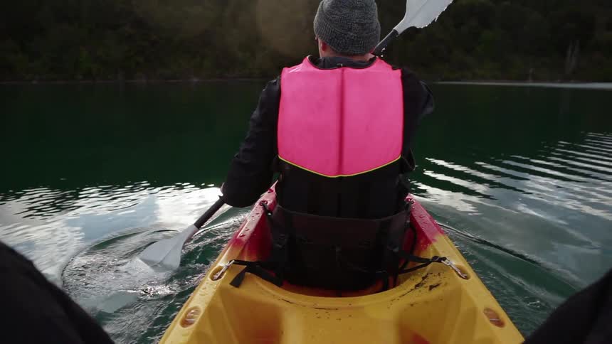 A man is rowing a canoe on a cloudy day as another sits behind him