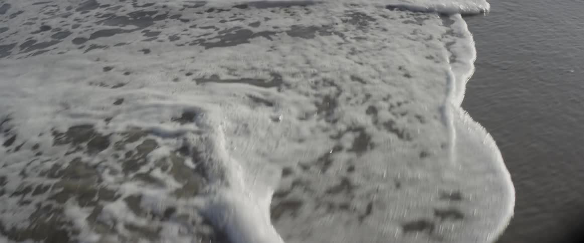 The waves hitting the sand cause small bubbles