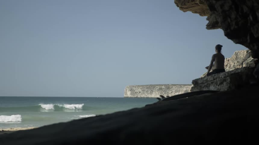 Woman sits on a rock near the ocean under a blue sky