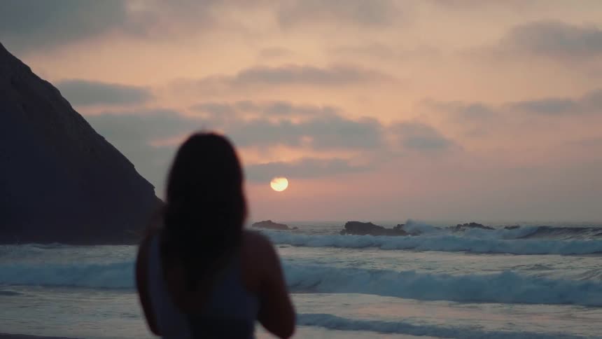 A woman is watching the sun go down at a beach