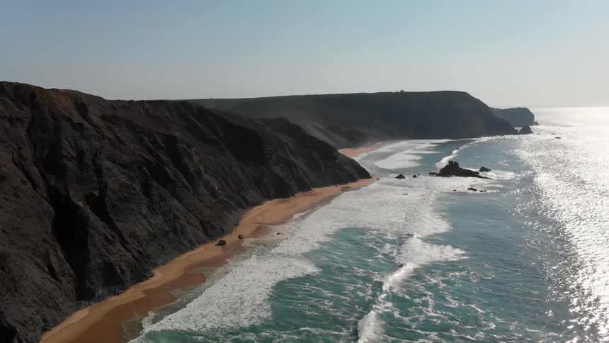The waves hit the shore by the rocky cliffs