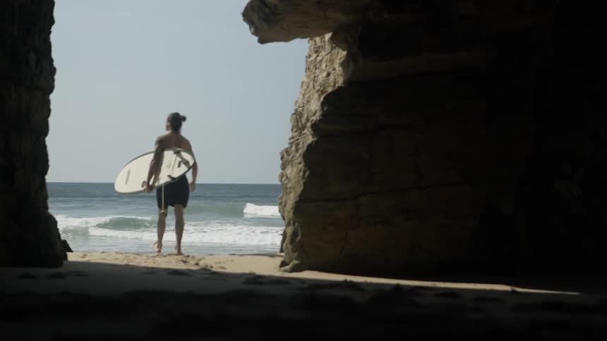 A surfer carries a surfboard on a beach