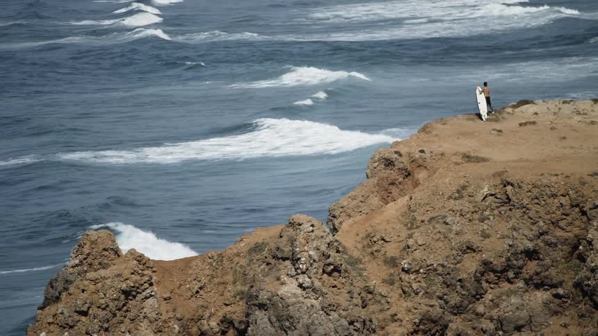 Man with a surfboard watches the waves approach