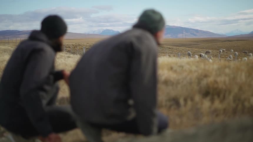 Two men crouch near a field