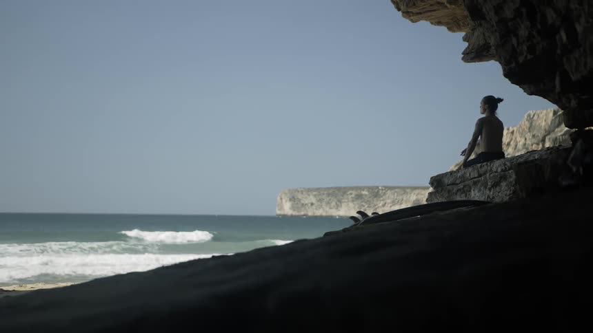 A surfer sits on a beach