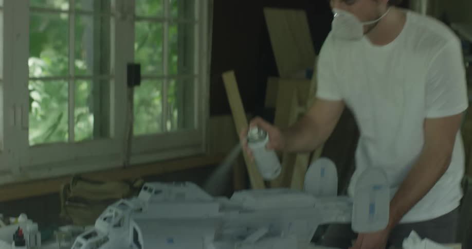 A man wears a mask as he spray paints a model
