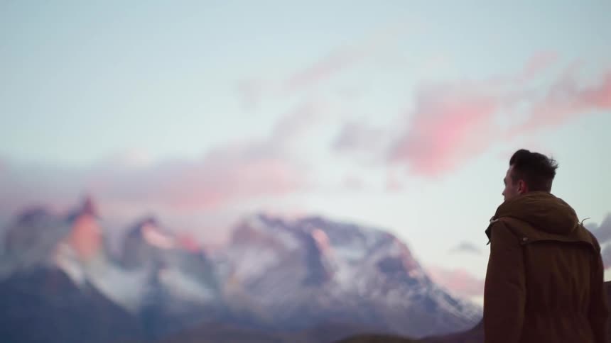 A man stands outside looking at a mountain on a windy day