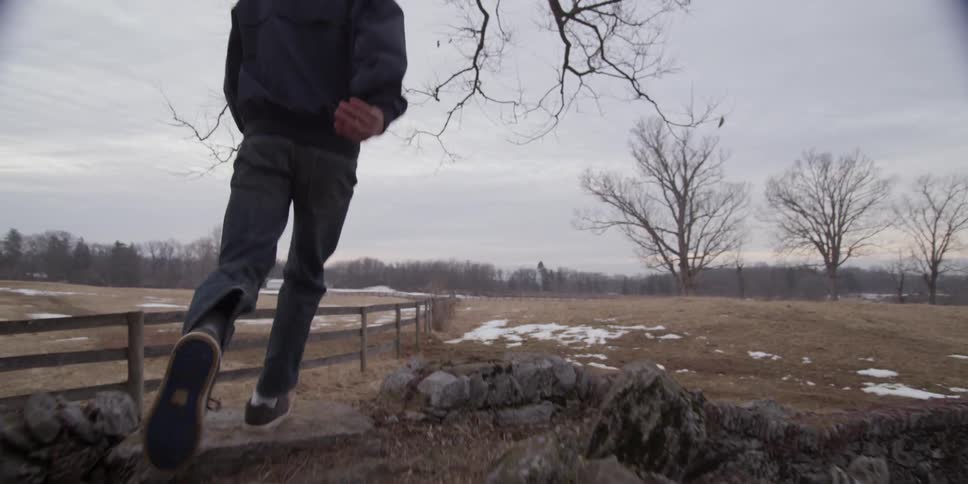 Boy running up some stones onto a field on a cloudy day