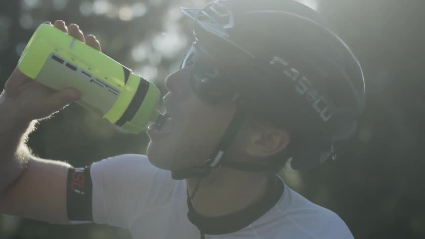 A man pours water over his helmet and takes a drink