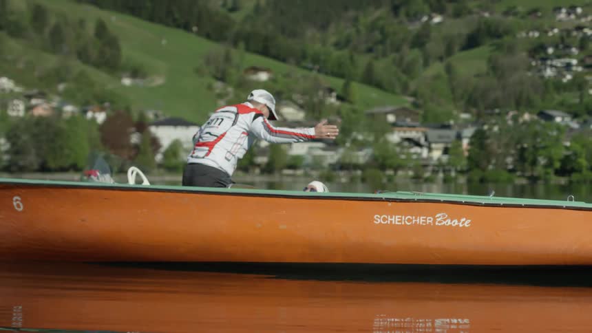 Man stands and gestures while riding in a small orange boat