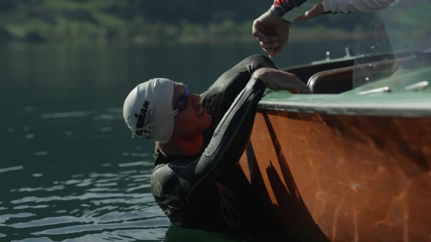 A coach talking to a swimmer is gesturing to his watch as they float in a lake in daylight