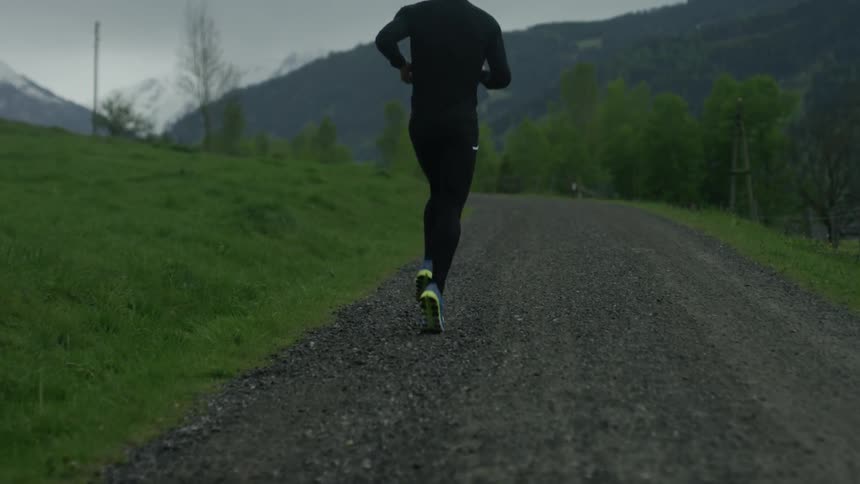 A man jogs down a path through green grass and trees