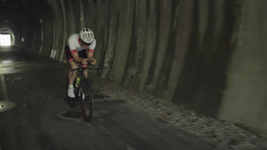 A man is riding a bicycle through a tunnel in daylight