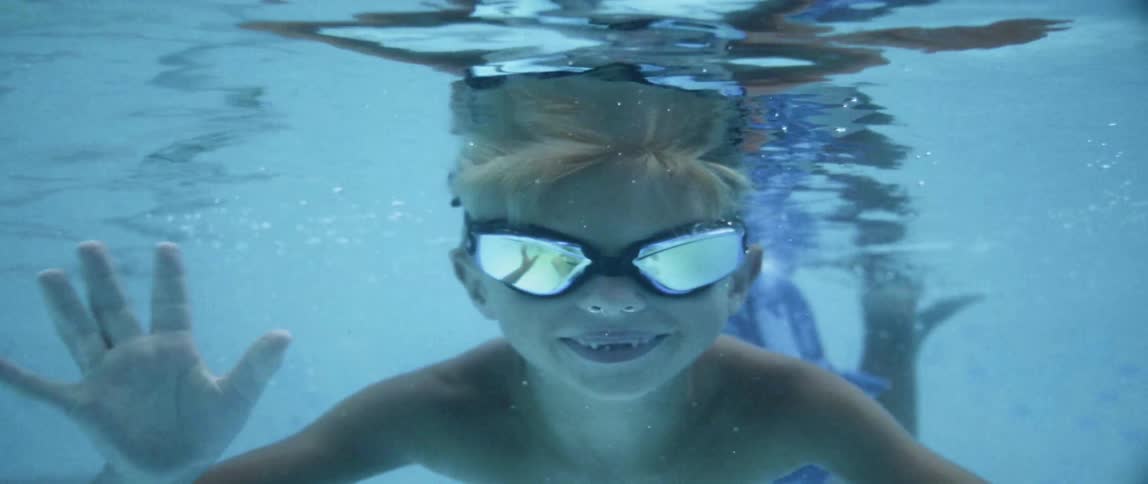 A boy waves while swimming underwater