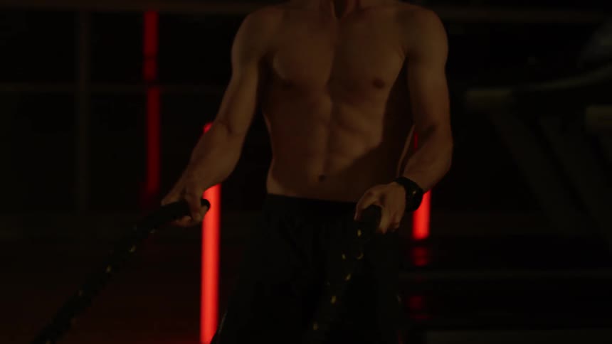 A man is lifting ropes and breathing heavy in the gym