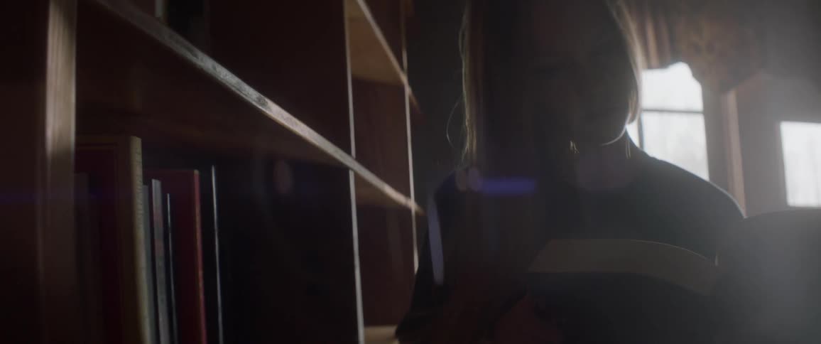 A woman reads a book next to a bookshelf