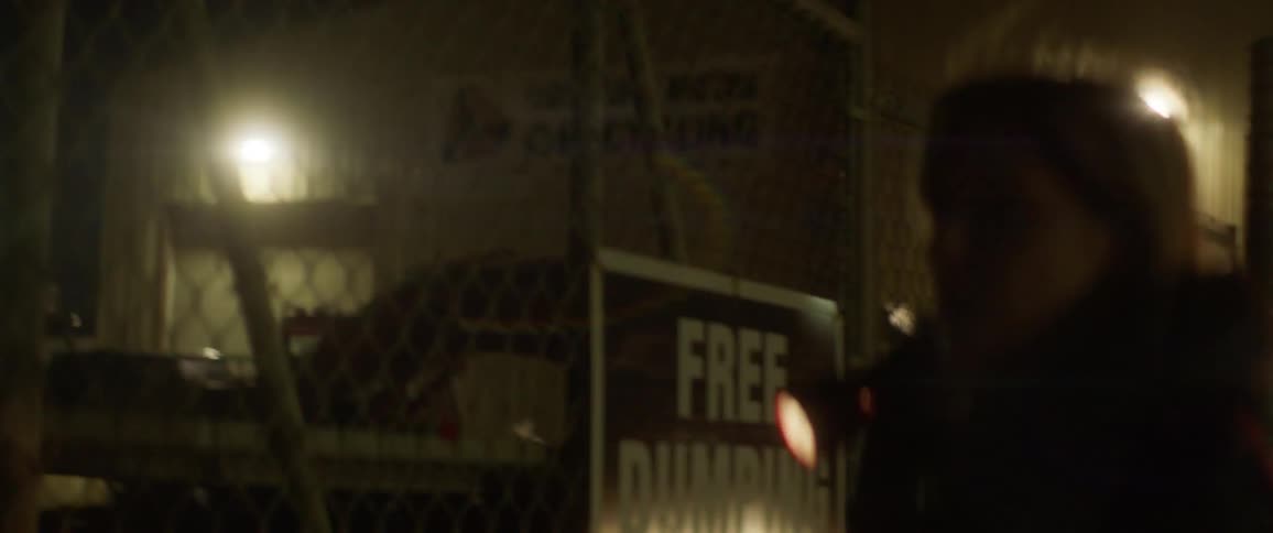 A woman shines a flashlight through a chain link fence