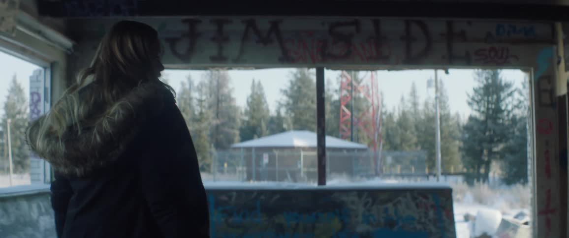 A girl walks around a graffiti covered building on a winter day