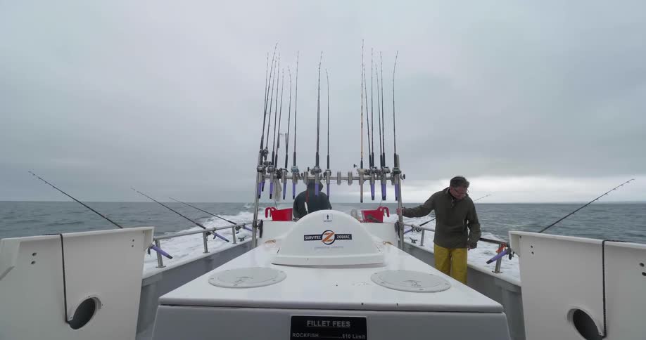 Men are standing on a fishing boat as it sails in the ocean on a cloudy day