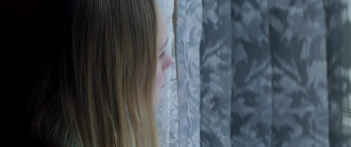 Young girl looks through a window with drapes