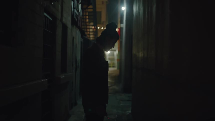 A man stands in an alley looking down and talking to himself
