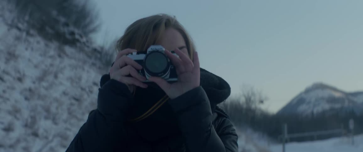 A woman is smiling as she takes a photo in the snow