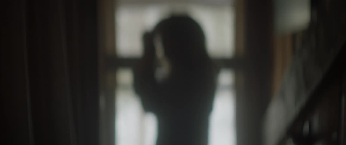 A woman is worrying as she stands by a window inside in daylight