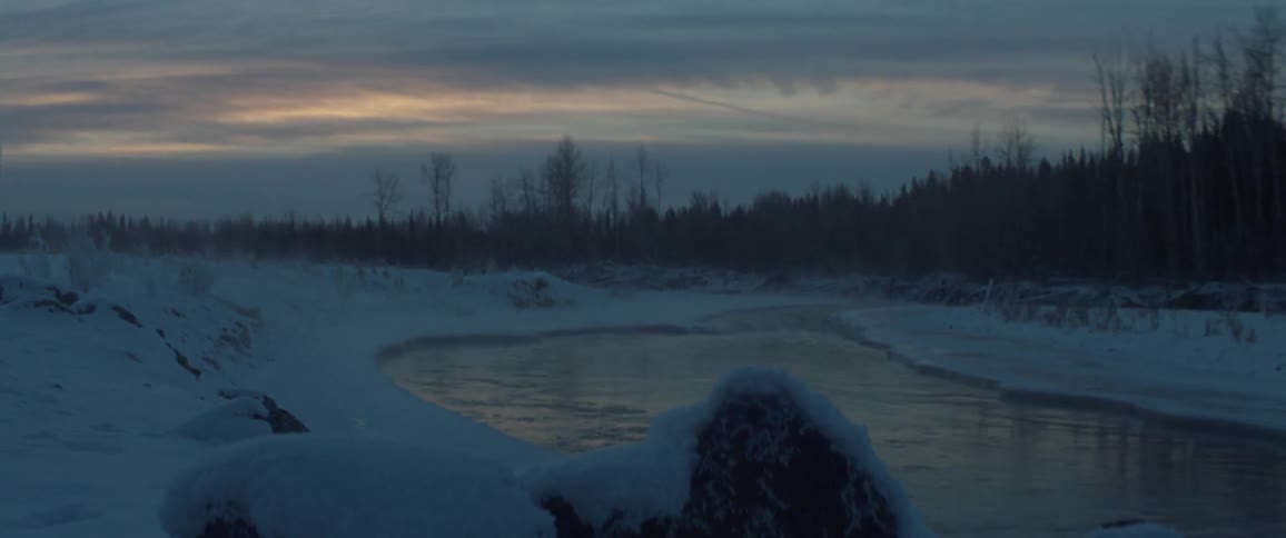 A river flows through a snowy landscape at dusk