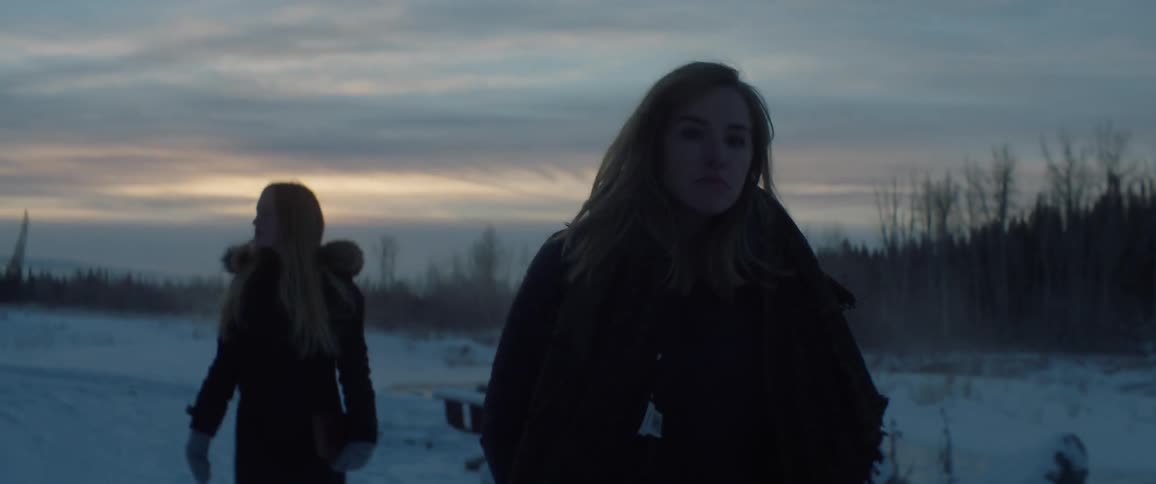 Two women walk on the snowy ground at sunset