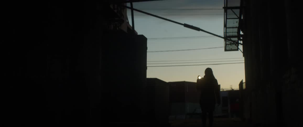 A woman walks by an industrial building with a flashlight