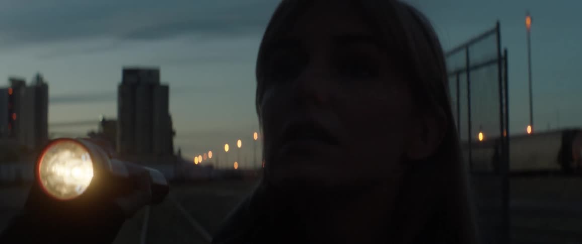 A woman is shining a flashlight outside at dawn