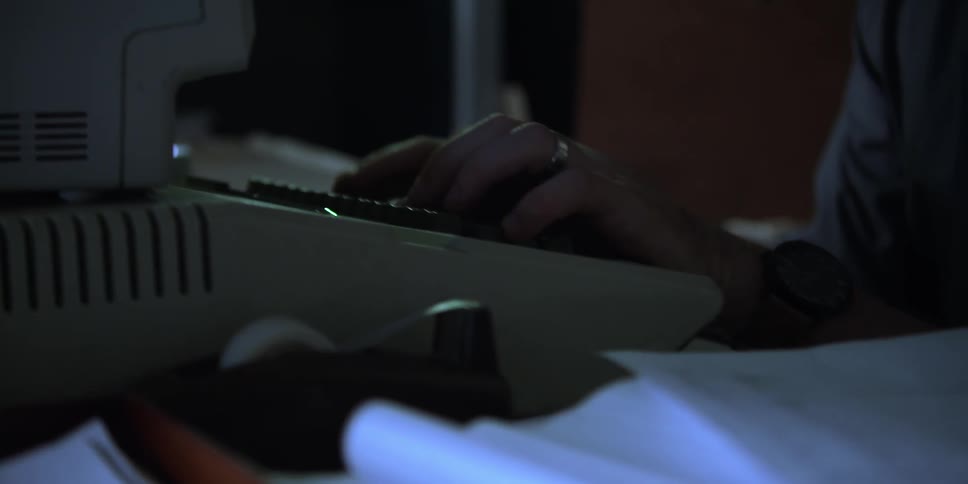 Hands type on an old computer keyboard