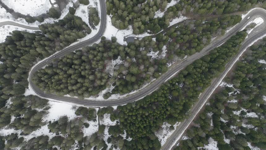 Cars travel on a road that loops and winds through trees and snow