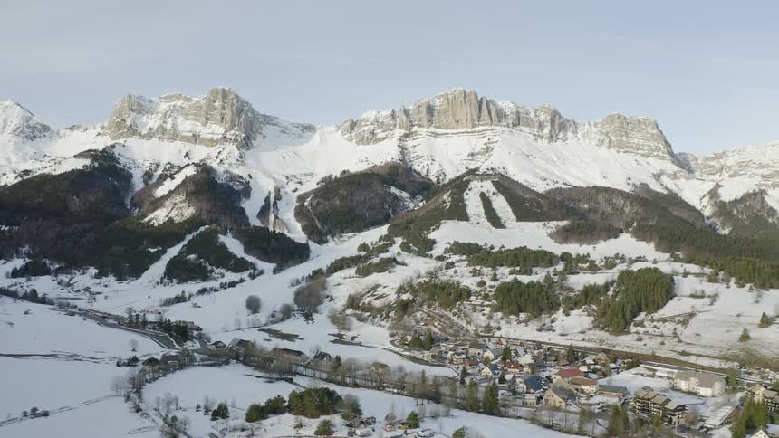 A village is sitting nestled in the valley of a mountain range in winter