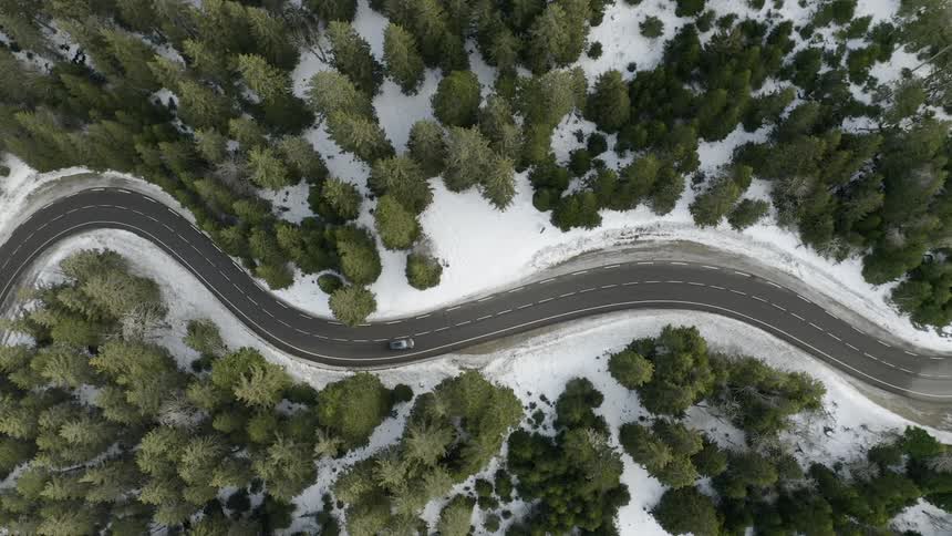 Vehicle drives down a winding snow and tree lined road