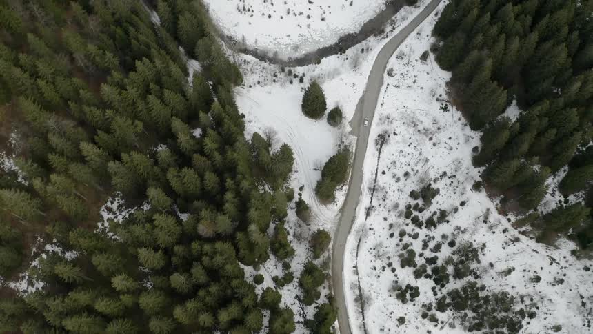 A vehicle is driving on a winding road in a natural landscape in winter