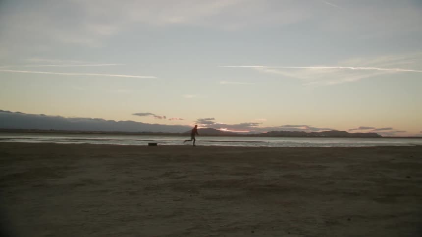 A person runs and drags a tire on a beach at sunset