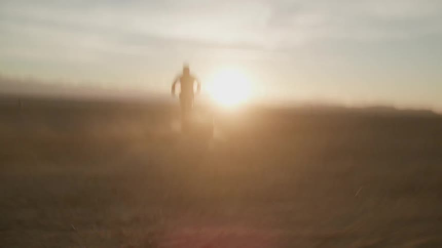 Person run across flat dirt land towards the sun