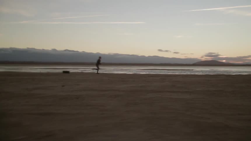 A female athlete is pulling a tire as she runs across a beach at dusk