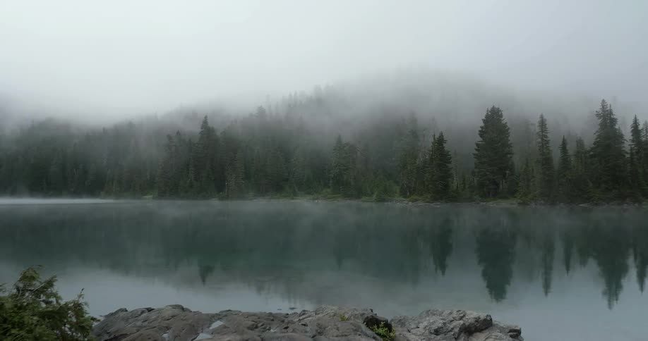 Lake surrounded by foggy hills and trees