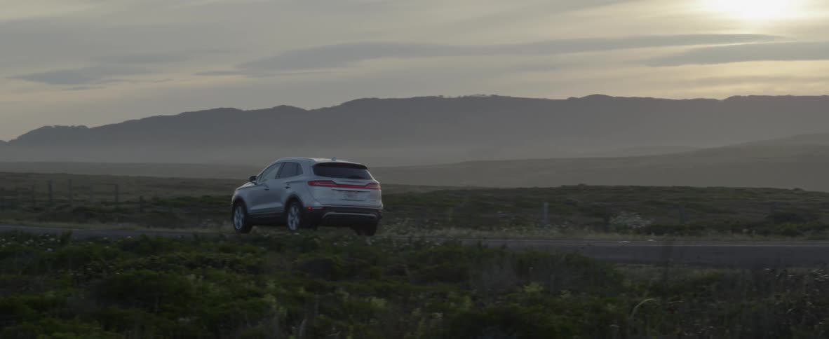 A vehicle is driving on a rural road at dusk