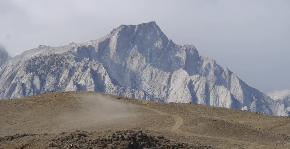 Vehicles drive on a dirt road towards mountains