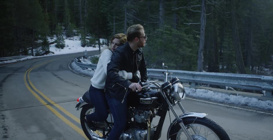 A man and woman ride a motorcycle in a forest
