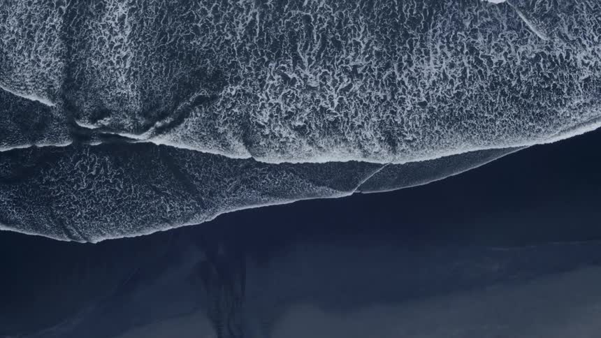Waves are rolling onto a black beach in daylight